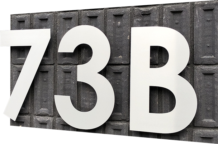 Große Edelstahl Hausnummer 73B montiert auf einer strukturierten dunklen Ziegelfassade