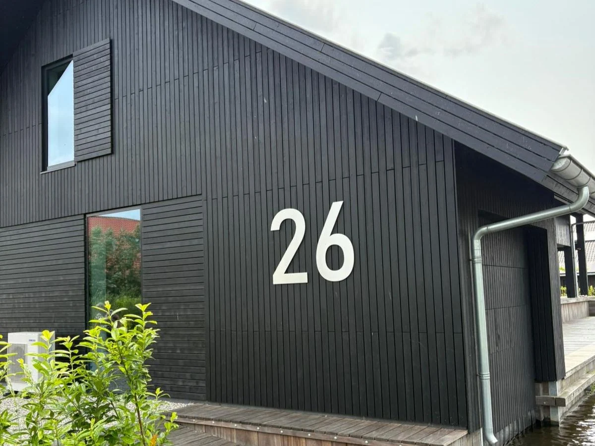 Edelstahl Hausnummer 26 an dunkler Holzfassade – klare Typografie in Bahnschrift