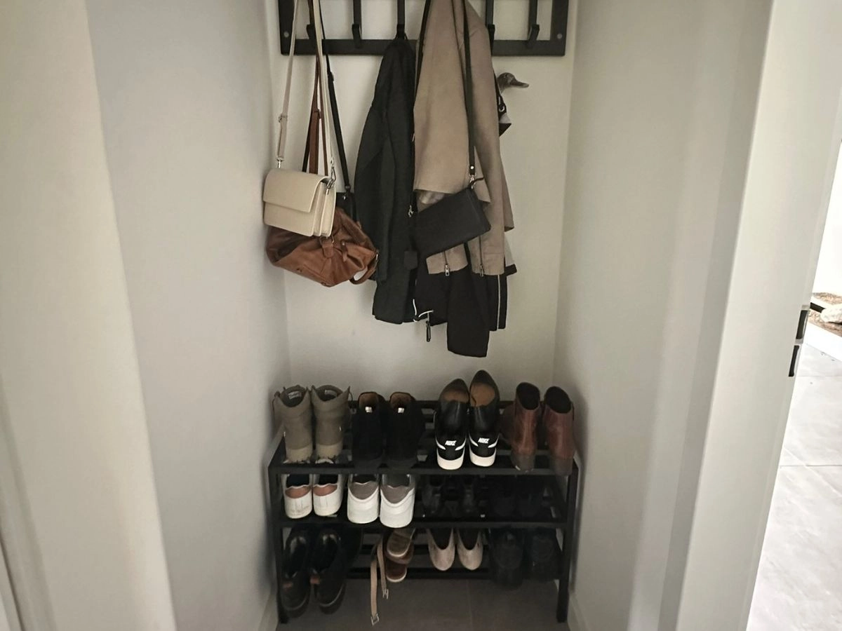 Kompaktes Edelstahl-Schuhregal in Schwarz, perfekt eingepasst in eine schmale Garderoben-Nische unter Jacken und Taschen