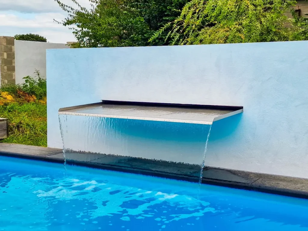 Edelstahl Wasserfall Modell Livingstone, 180 cm breit, bündig eingebaut in weiße Gartenmauer über einem Pool