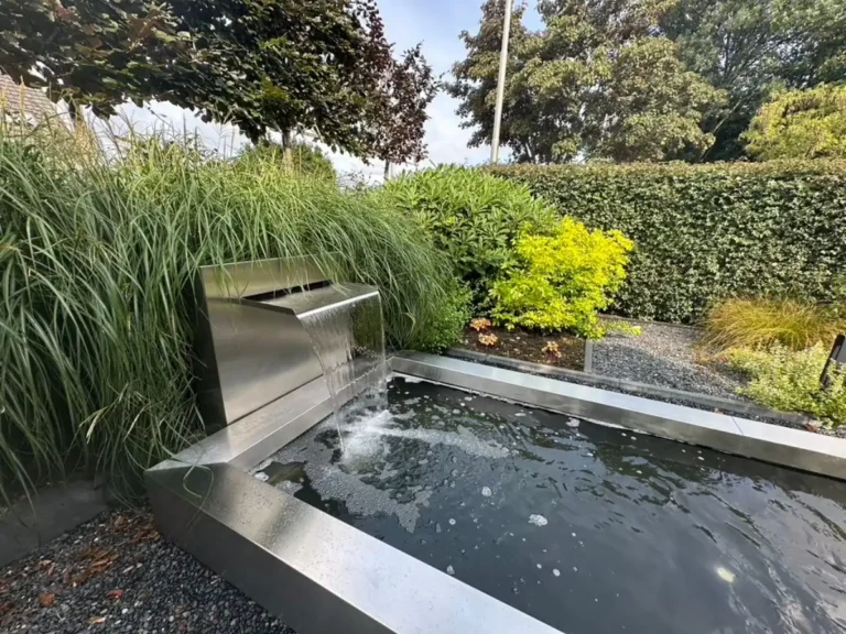 Moderner Garten mit breitem Edelstahl-Wasserfall an einem rechteckigen Teich mit Ziergräsern