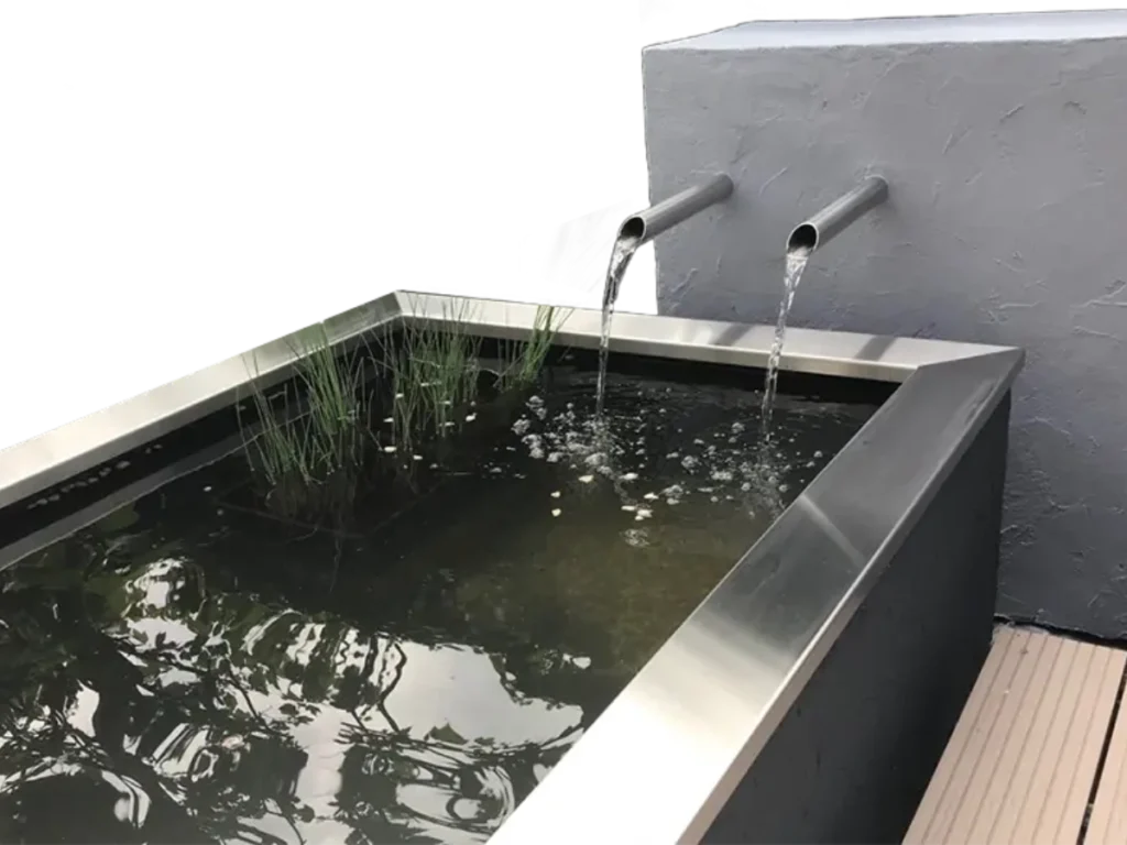 Moderner gerader Edelstahl-Wasserauslauf mit klarem Wasserfluss in einen Gartenteich