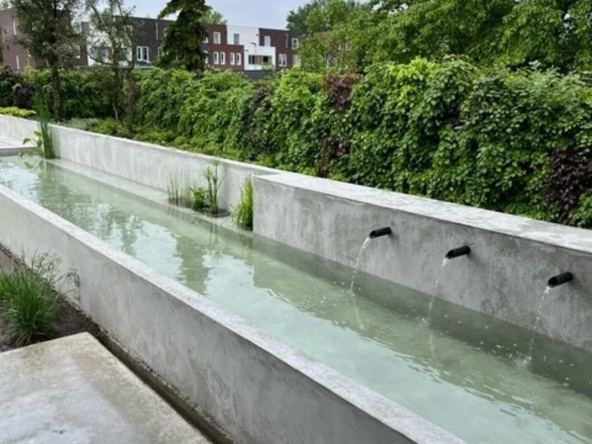 Mehrere gerade Edelstahl-Wasserausläufe in lange Gartenmauer mit modernem Gartenteich
