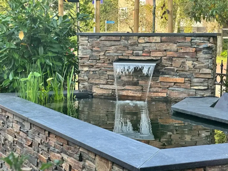Edelstahl-Wasserfall mit LED-Beleuchtung in Natursteinmauer, gespiegelt im Wasser des Teichs